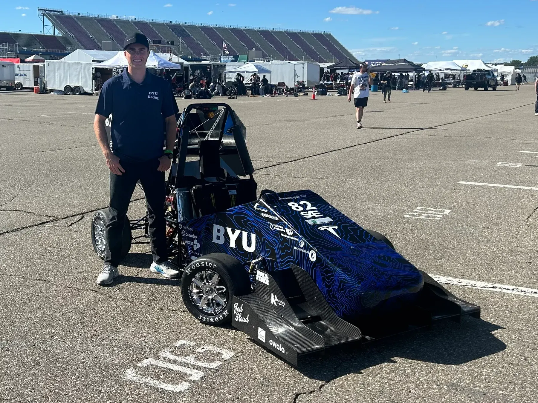 Carson beside the BYU Racing electric racecar at competition